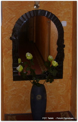 Duży, wysoki wazon ze sztucznymi, białymi różami, na tle lustra.
